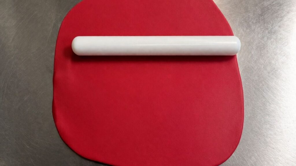 Rolled out pink fondant with rolling pin on smooth surface ready for cutting fondant baby shoes