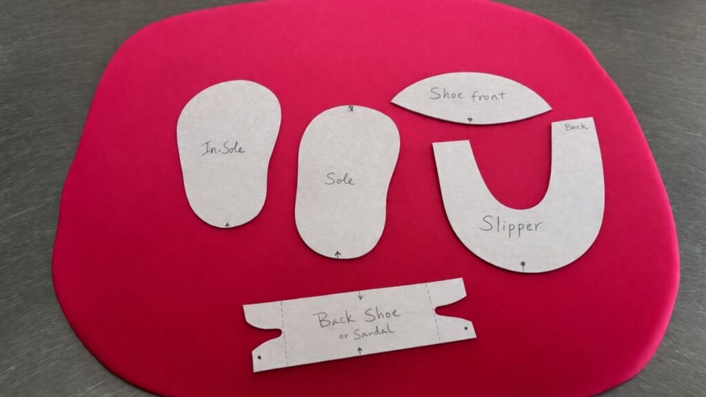 Paper template pieces placed on rolled out pink fondant ready to cut fondant baby shoes