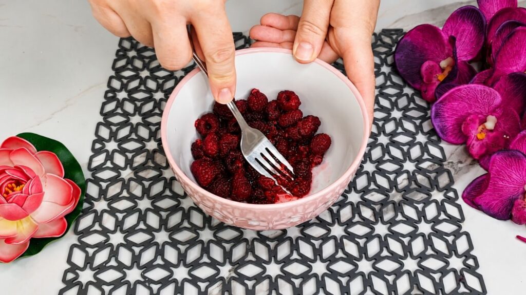 Crushing fresh raspberries with sugar and water for easy no bake raspberry yogurt cake glaze topping