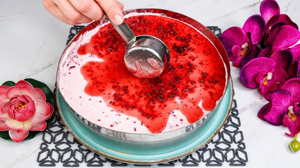 Pouring raspberry glaze over chilled no bake raspberry yogurt cake filling in springform pan