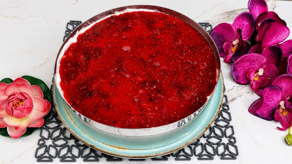 Pouring raspberry glaze over chilled no bake raspberry yogurt cake filling in springform pan