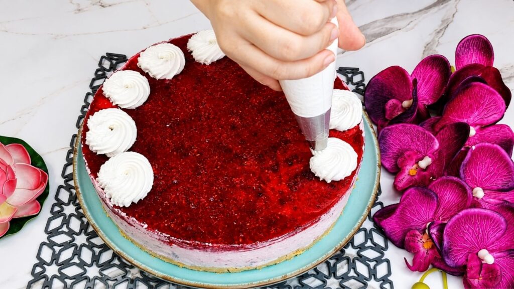 Decorating easy no bake raspberry yogurt cake with whipped cream fresh raspberries and mint leaves