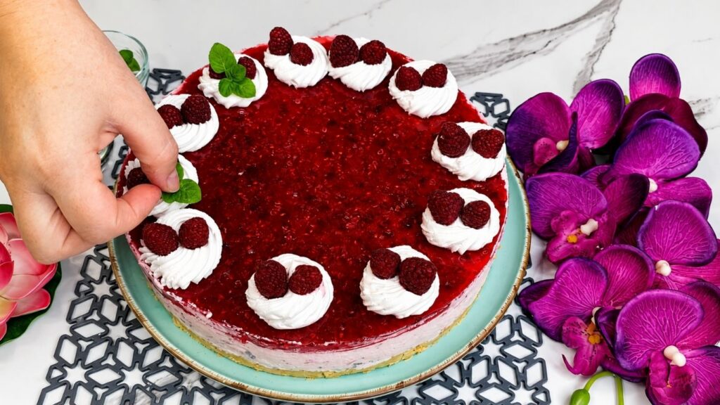 Decorating easy no bake raspberry yogurt cake with whipped cream fresh raspberries and mint leaves