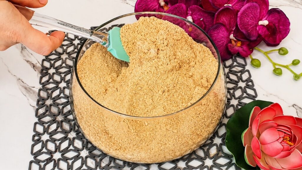 Mixing crushed graham crackers with milk and sugar for no bake raspberry yogurt cake recipe crust base