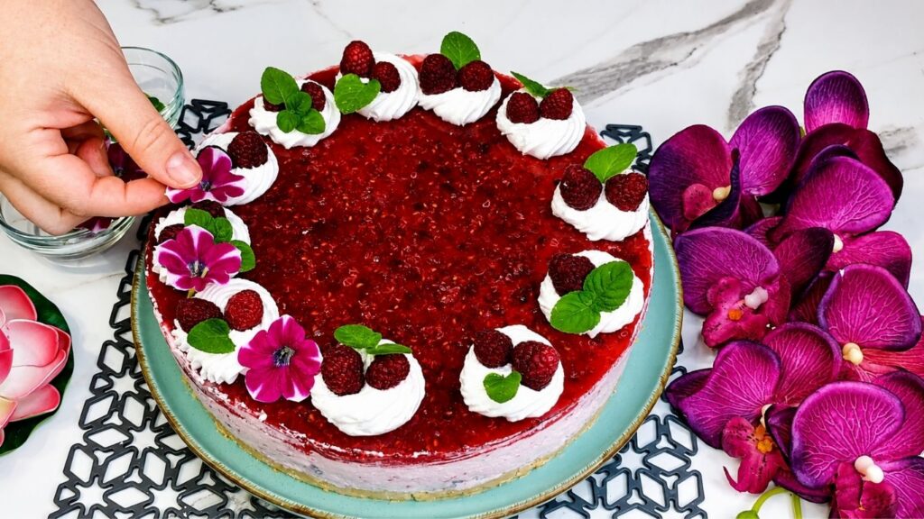 Decorating easy no bake raspberry yogurt cake with whipped cream fresh raspberries and mint leaves