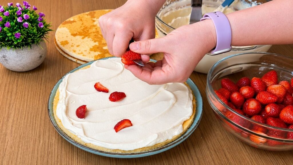 Adding chopped fresh strawberries over the first layer of vanilla cream for easy strawberry cake filling