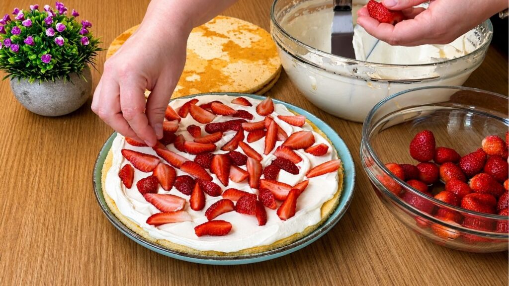 Adding chopped fresh strawberries over the first layer of vanilla cream for easy strawberry cake filling