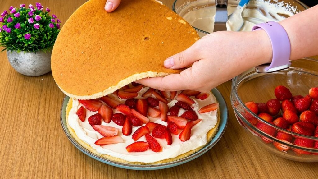 Placing the second sponge cake layer over strawberries and vanilla cream for easy strawberry cake assembly