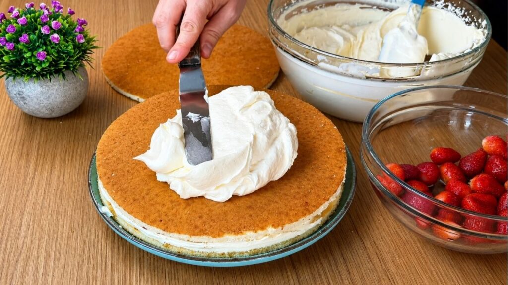 Spreading creamy vanilla filling over sponge cake layers for easy strawberry cake assembly