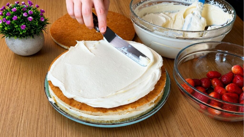 Spreading creamy vanilla filling over sponge cake layers for easy strawberry cake assembly