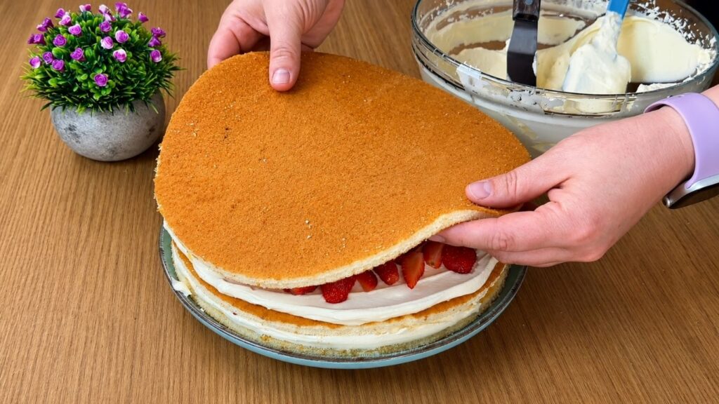 Placing the final sponge cake layer on top of the filled easy strawberry cake before decorating
