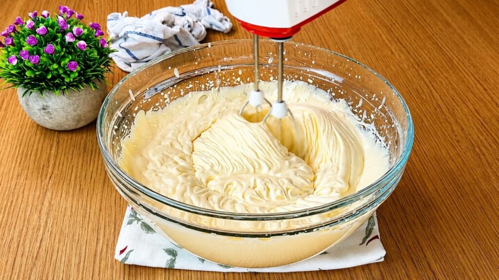 Mixing vanilla cream with a hand mixer for easy strawberry cake filling until smooth and creamy