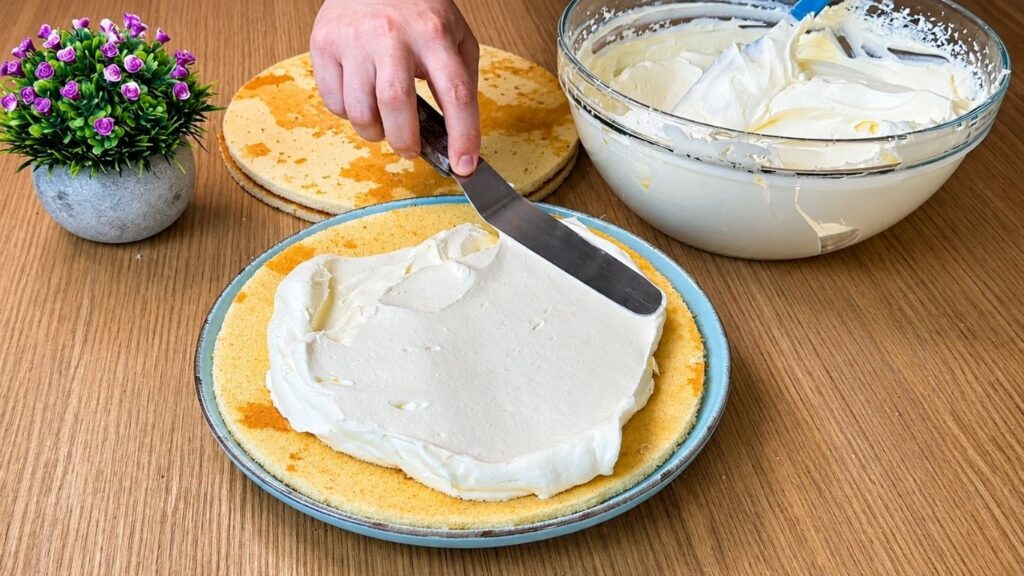 Spreading creamy vanilla filling over sponge cake layers for easy strawberry cake assembly