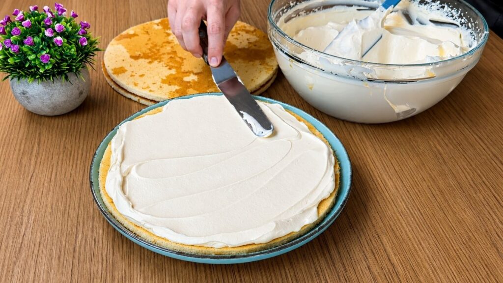 Spreading creamy vanilla filling over sponge cake layers for easy strawberry cake assembly