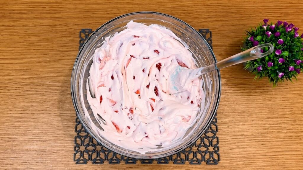Pouring the whipped strawberry yogurt filling over the chilled cookie crust in the springform pan and smoothing the top into an even layer.