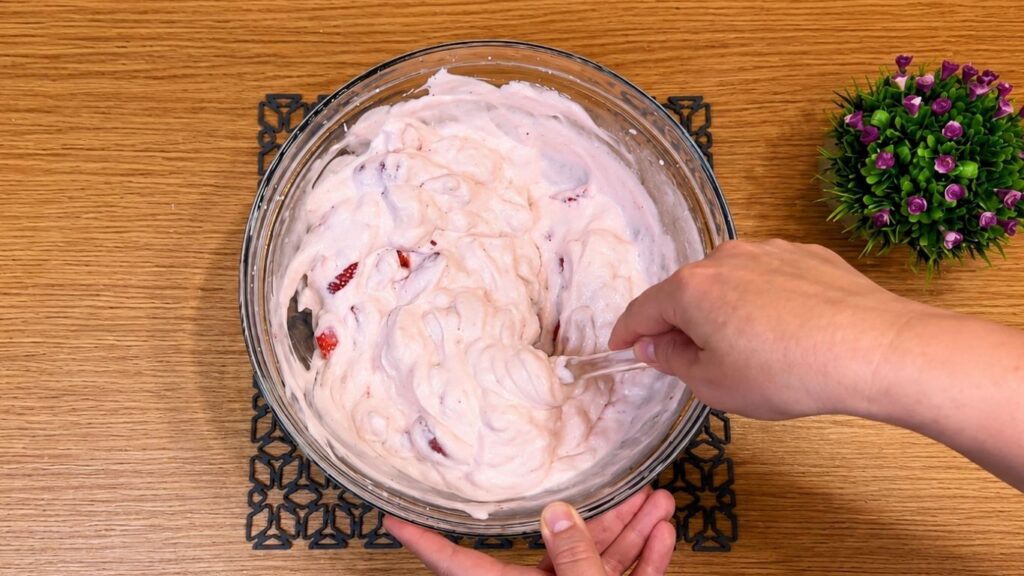 Pouring the whipped strawberry yogurt filling over the chilled cookie crust in the springform pan and smoothing the top into an even layer.