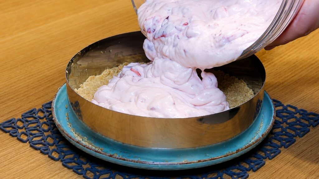 Pouring the whipped strawberry yogurt filling over the chilled cookie crust in the springform pan and smoothing the top into an even layer.