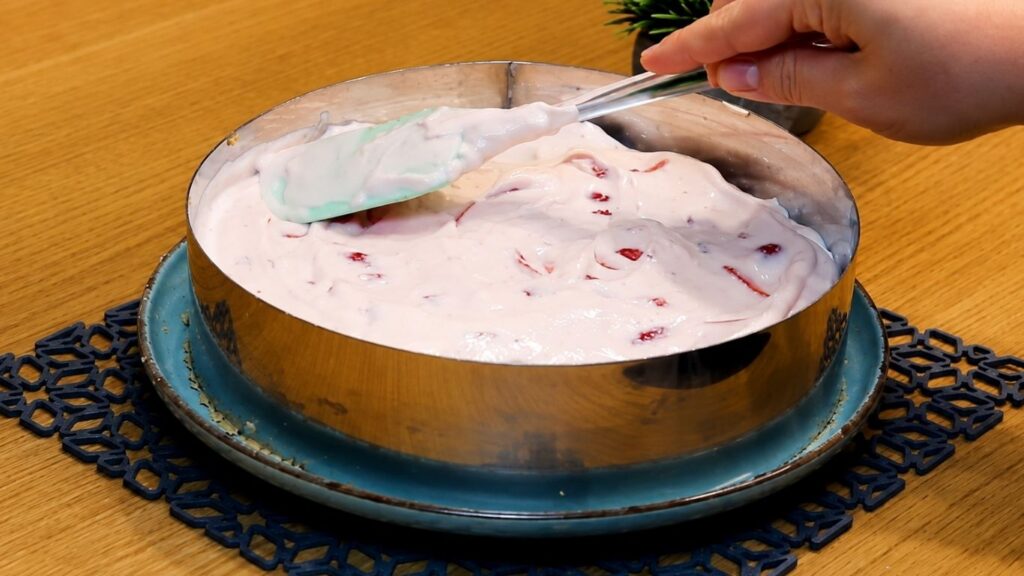 Pouring the whipped strawberry yogurt filling over the chilled cookie crust in the springform pan and smoothing the top into an even layer.