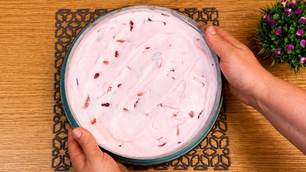 Pouring the whipped strawberry yogurt filling over the chilled cookie crust in the springform pan and smoothing the top into an even layer.