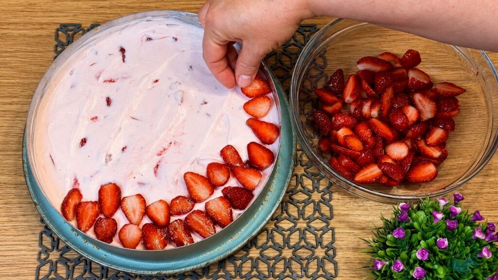 Slicing strawberries and arranging them neatly over the chilled no-bake strawberry yogurt cake before adding the glaze.