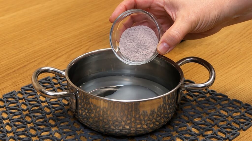 Preparing the strawberry cake glaze in a small saucepan by stirring water, sugar, and gelatin-based cake glaze mix until it just comes to a boil.
