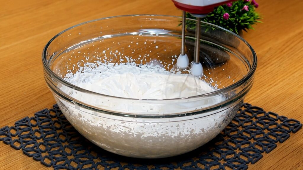 Whipping heavy cream until it becomes light and fluffy and holds stiff peaks for decorating the no-bake strawberry yogurt cake