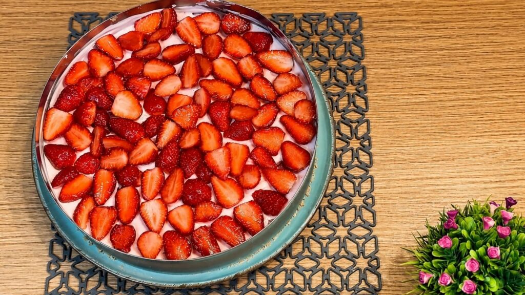 Slicing strawberries and arranging them neatly over the chilled no-bake strawberry yogurt cake before adding the glaze.