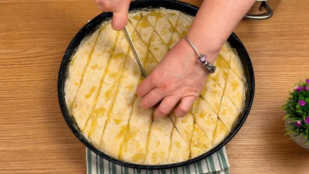 Cutting baklava into pieces before baking so the syrup can soak into every layer.