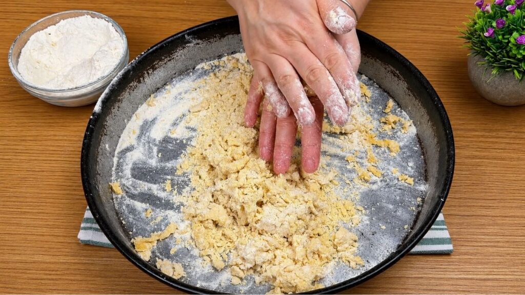 Hands rubbing flour, butter, and egg together to make homemade pastry crumbs for baklava recipe.