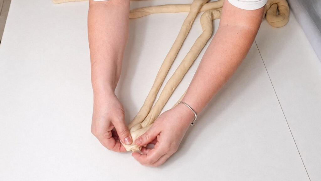 Braided dough being shaped into a Christmas bread wreath on a wooden work surface.