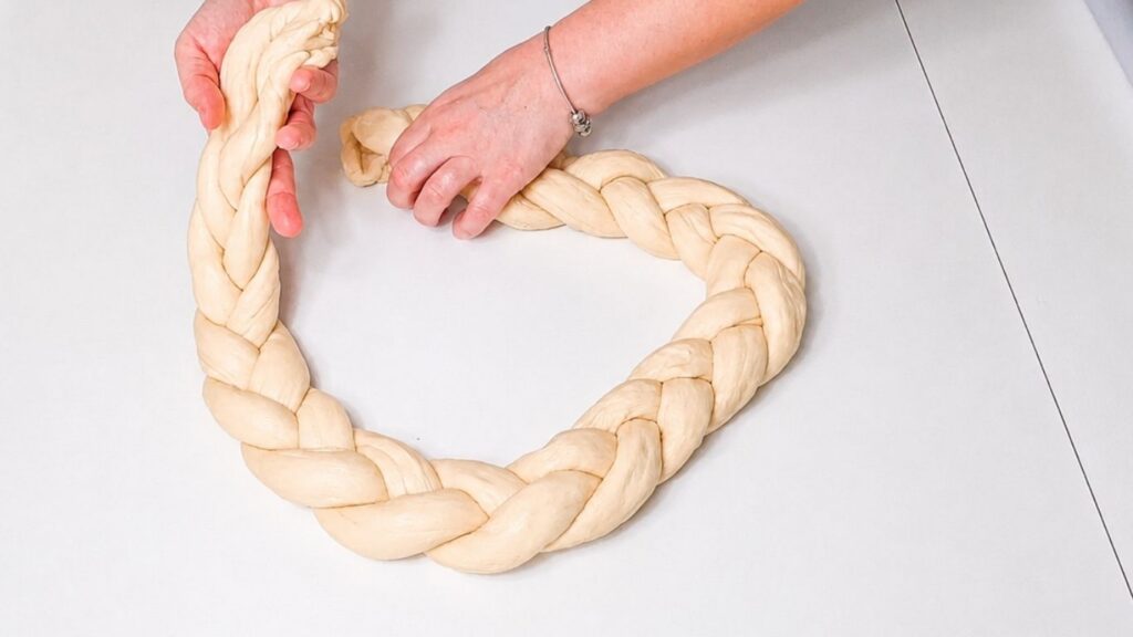 Braided dough being shaped into a Christmas bread wreath on a wooden work surface.
