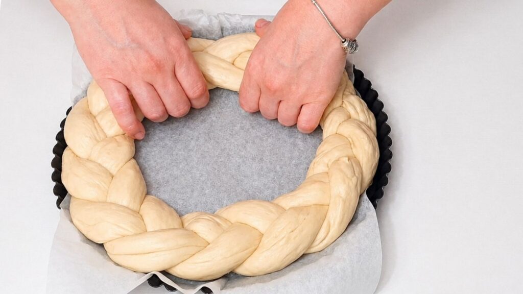 Braided Christmas bread wreath being placed into a baking pan lined with parchment paper.