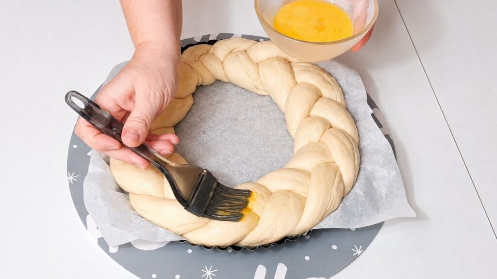 Christmas bread wreath in a baking pan brushed with egg wash before baking