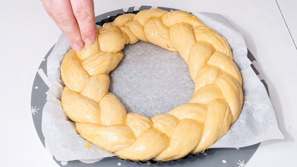Christmas bread wreath in a baking pan brushed with egg wash before baking