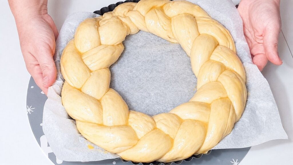 Christmas bread wreath in a baking pan brushed with egg wash before baking