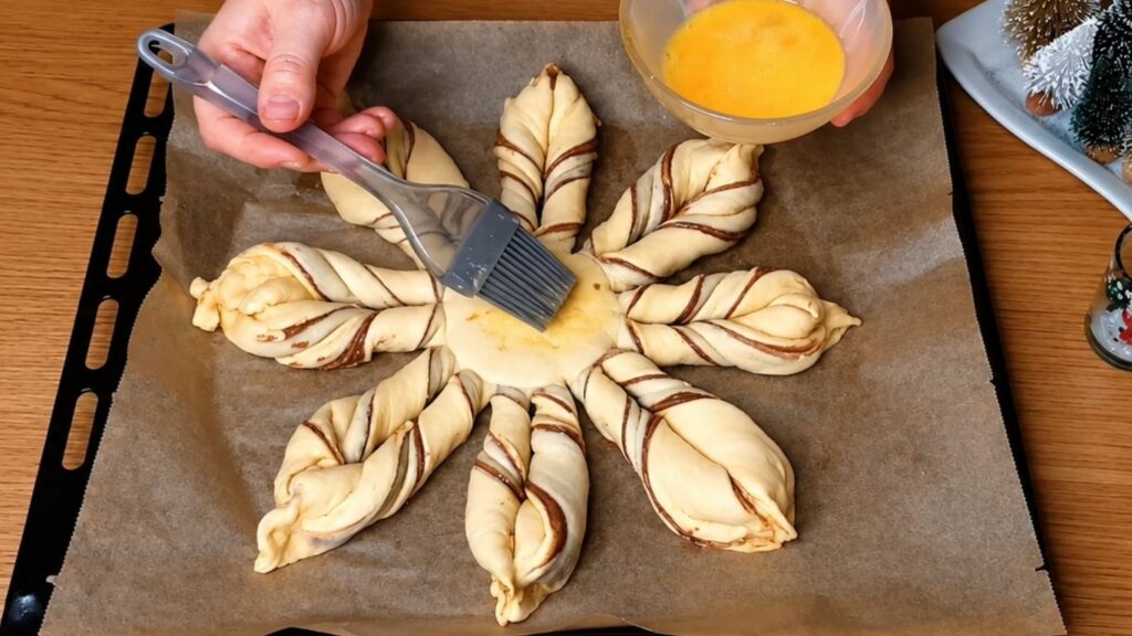 Brushing a beaten egg wash over an unbaked chocolate star bread using a pastry brush before baking