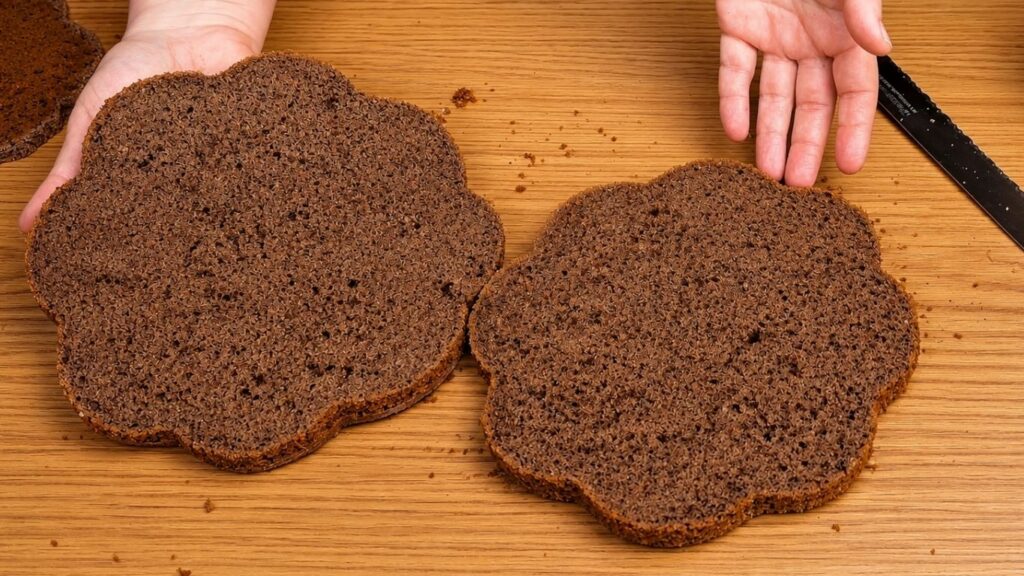 Chocolate sponge cake layer sliced in half, showing a soft, moist, and even texture ready for filling and stacking.