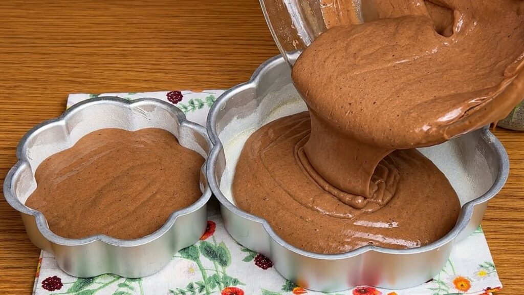 Pouring chocolate sponge cake batter into prepared cake pans before baking soft and moist cake layers.