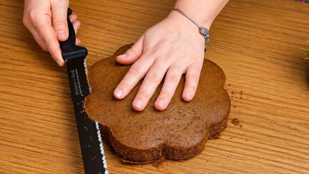 Trimming the top of a baked chocolate sponge cake with a knife to create an even cake layer for filling and stacking.