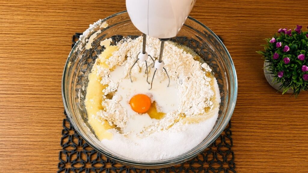 Mixing the vanilla sponge cake ingredients with a hand mixer until the batter comes together.