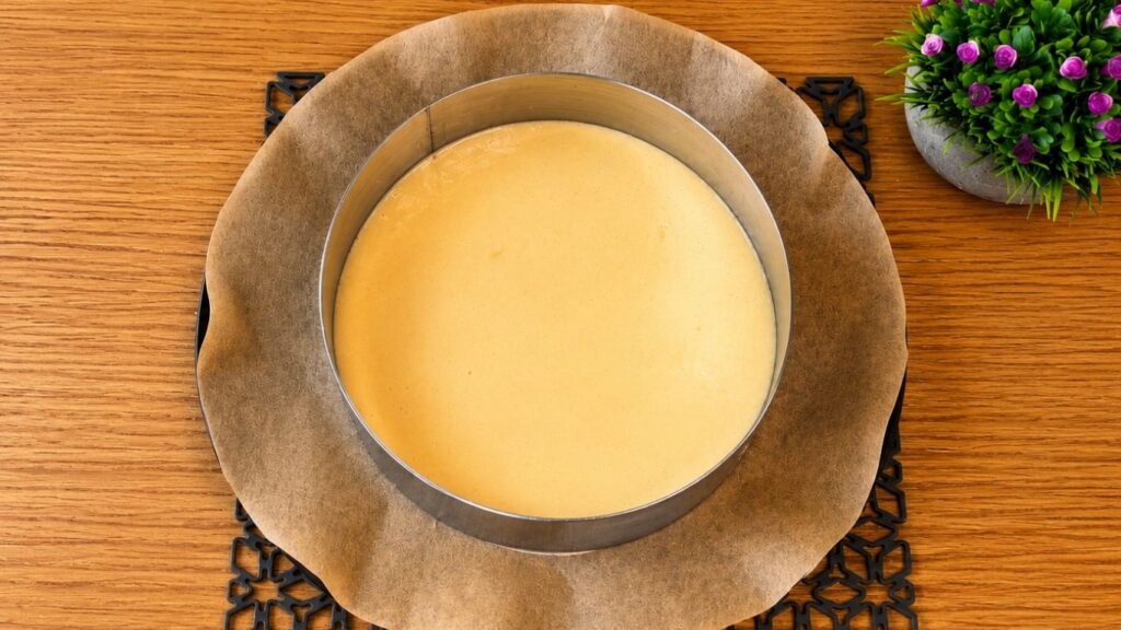 Pouring vanilla sponge cake batter into a prepared round cake pan.