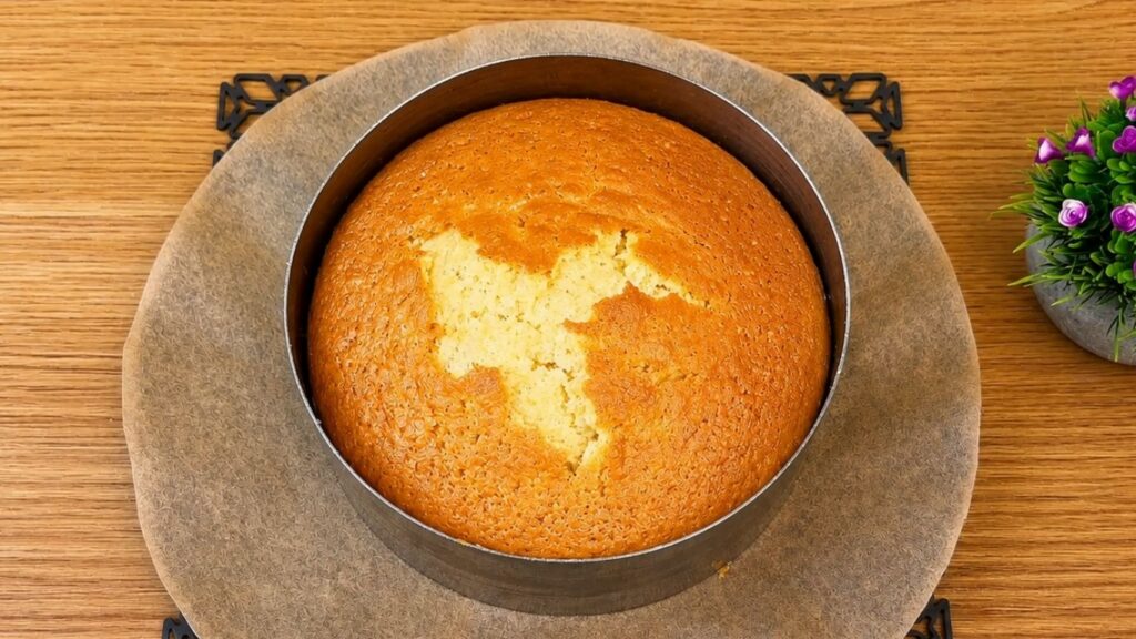 Baked vanilla sponge cake layer cooling in a round cake pan.
