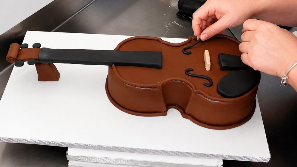 Adding fondant details to the violin body to make the realistic 3D violin cake look more lifelike.