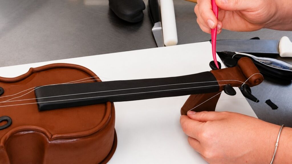 Adding decorative strings to the violin cake to create a realistic 3D instrument design.