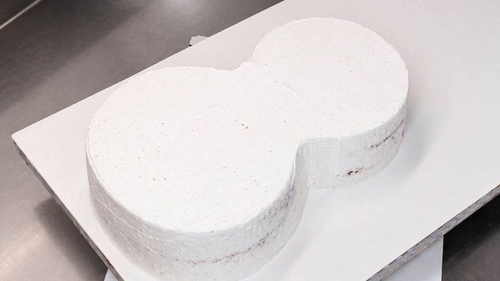 Applying buttercream to the carved chocolate cake base before covering the 3D violin cake with fondant.