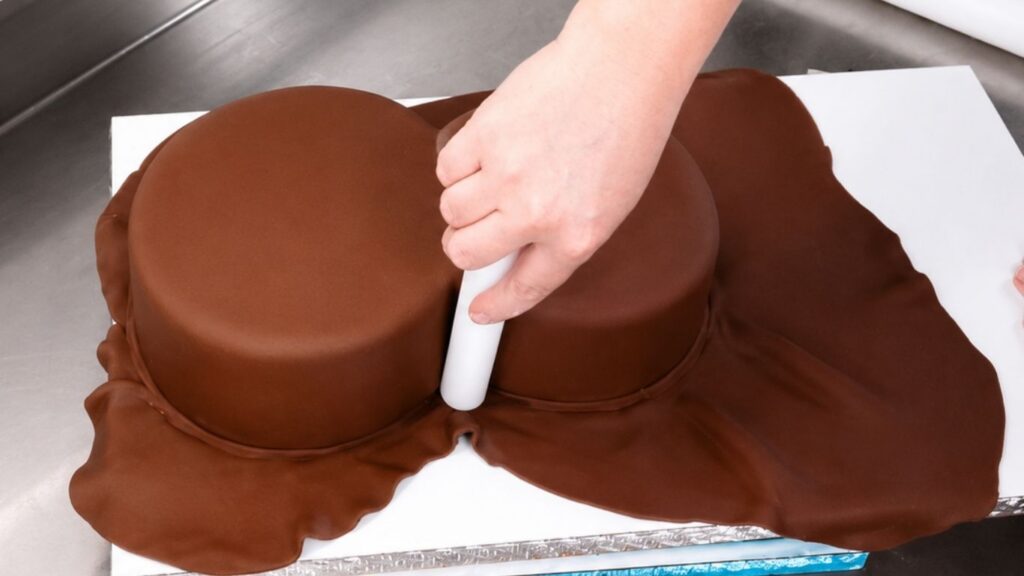 Smoothing brown fondant over the carved cake to create a clean base for a realistic 3D violin cake.