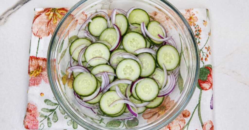 Thinly sliced English cucumber and red onion in a mixing bowl.