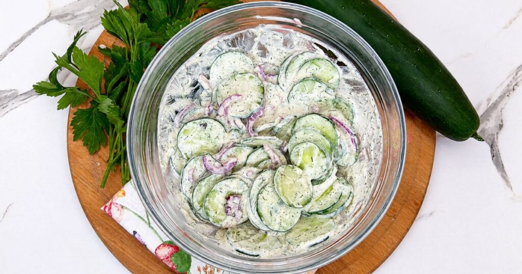 Creamy cucumber salad mixed in a bowl with thinly sliced cucumber, red onion, dill, and sour cream dressing.