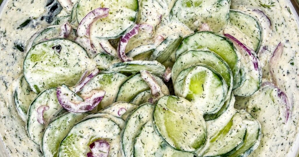 Creamy cucumber salad mixed in a bowl with thinly sliced cucumber, red onion, dill, and sour cream dressing.