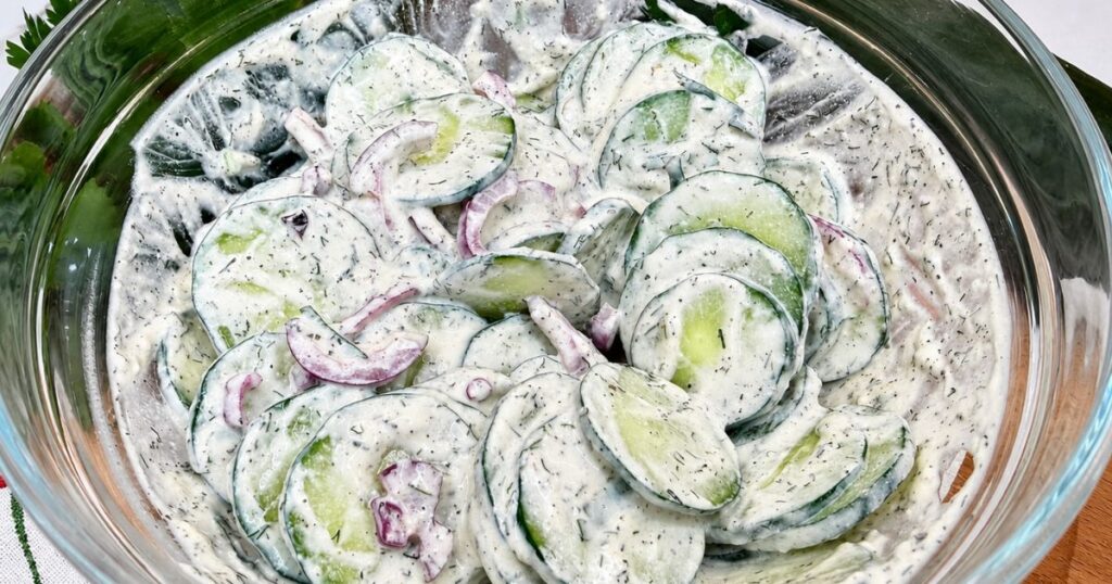 Creamy cucumber salad mixed in a bowl with thinly sliced cucumber, red onion, dill, and sour cream dressing.